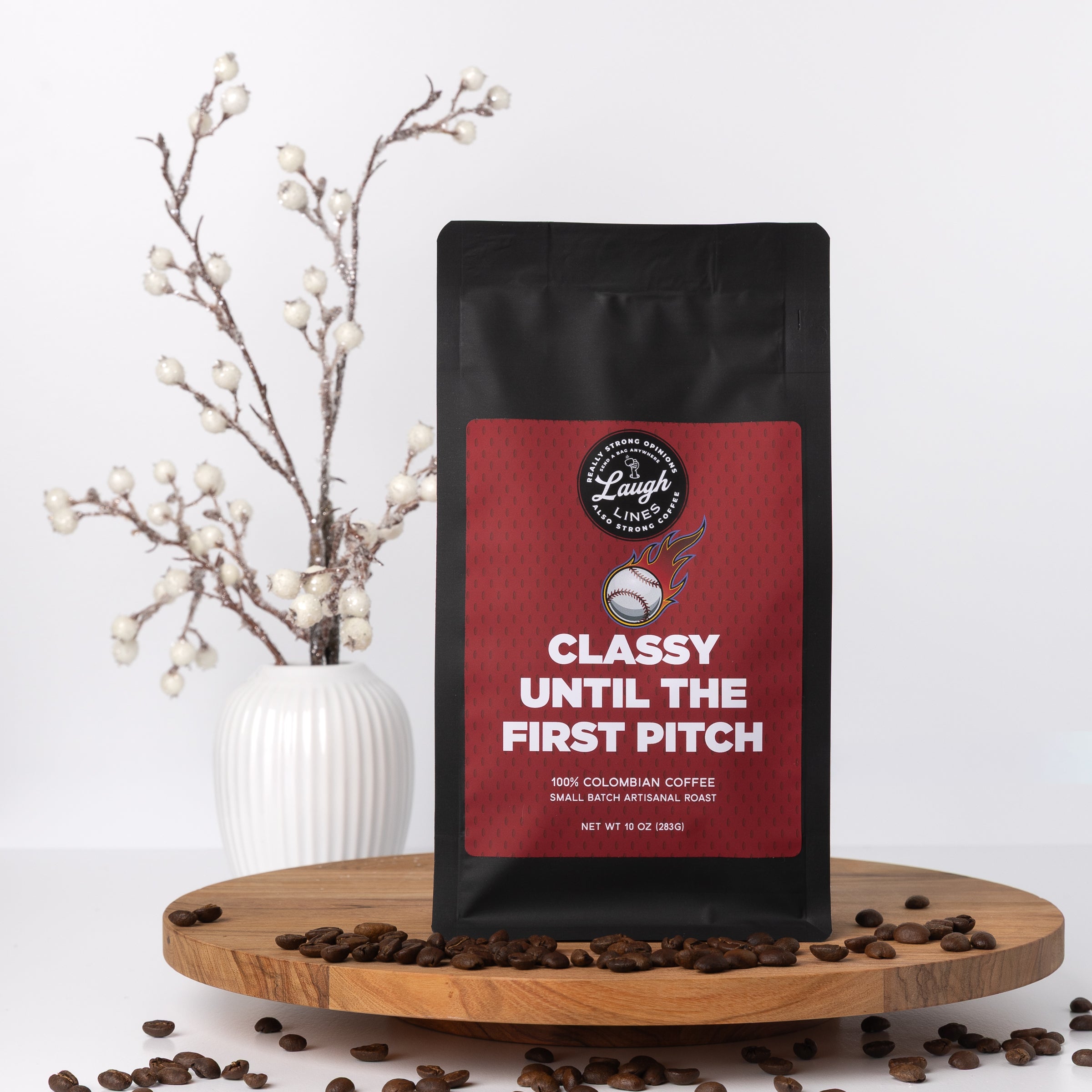 Coffee bag with a red label that says, "Classy Until the First Pitch," on a wooden stand with coffee beans and decorative branches.