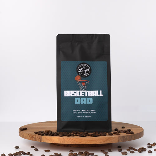 Coffee bag labeled 'Basketball Dad' on a wooden platform with coffee beans around, on a white background