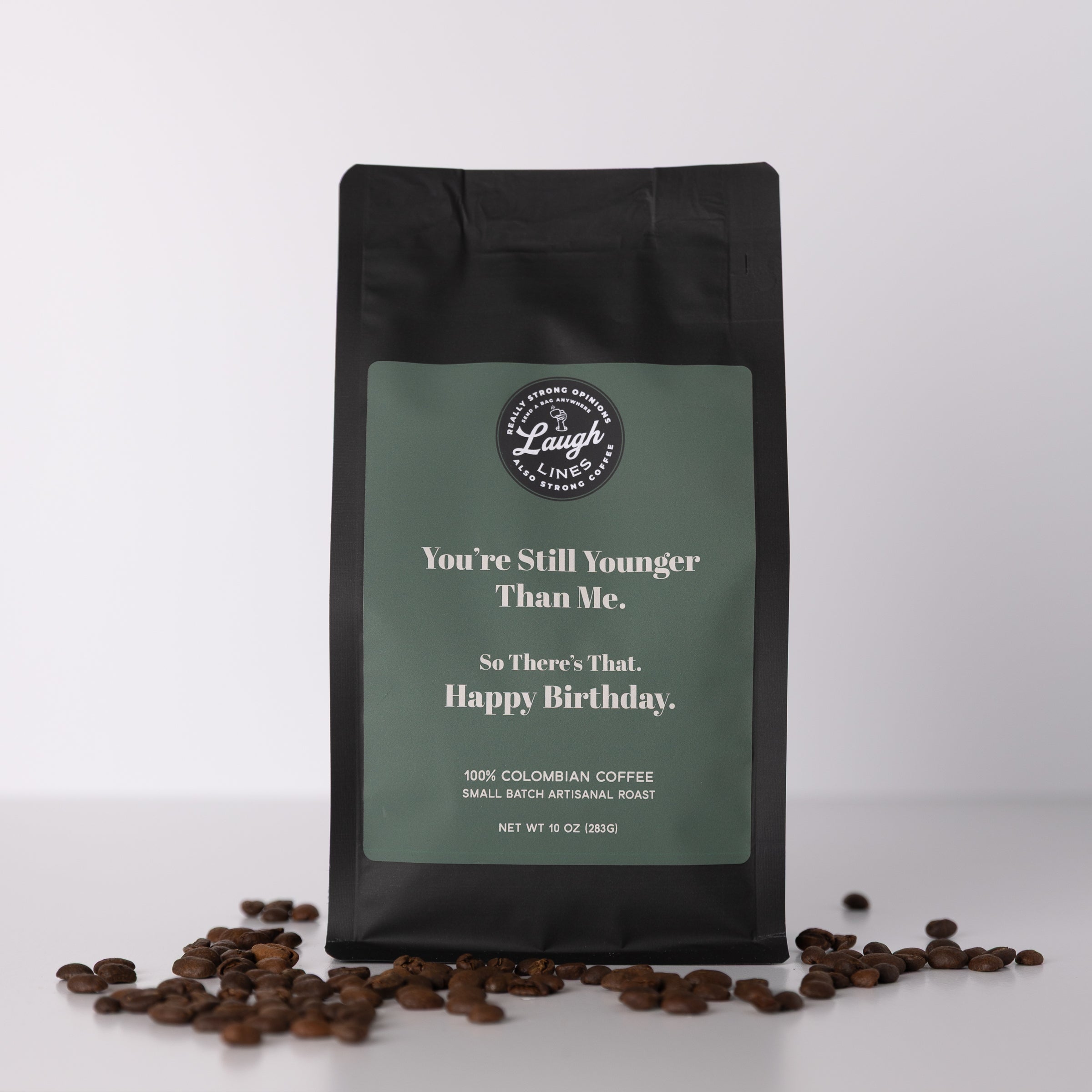 Coffee bag with humorous text that reads 'You're Still Younger Than Me. So There's That. Happy Birthday.' and coffee beans on a white background