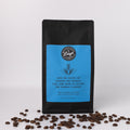 Coffee bag with blue label that reads Give me coffee to change the things I can and wine to change the things I cannot and coffee beans on a white background