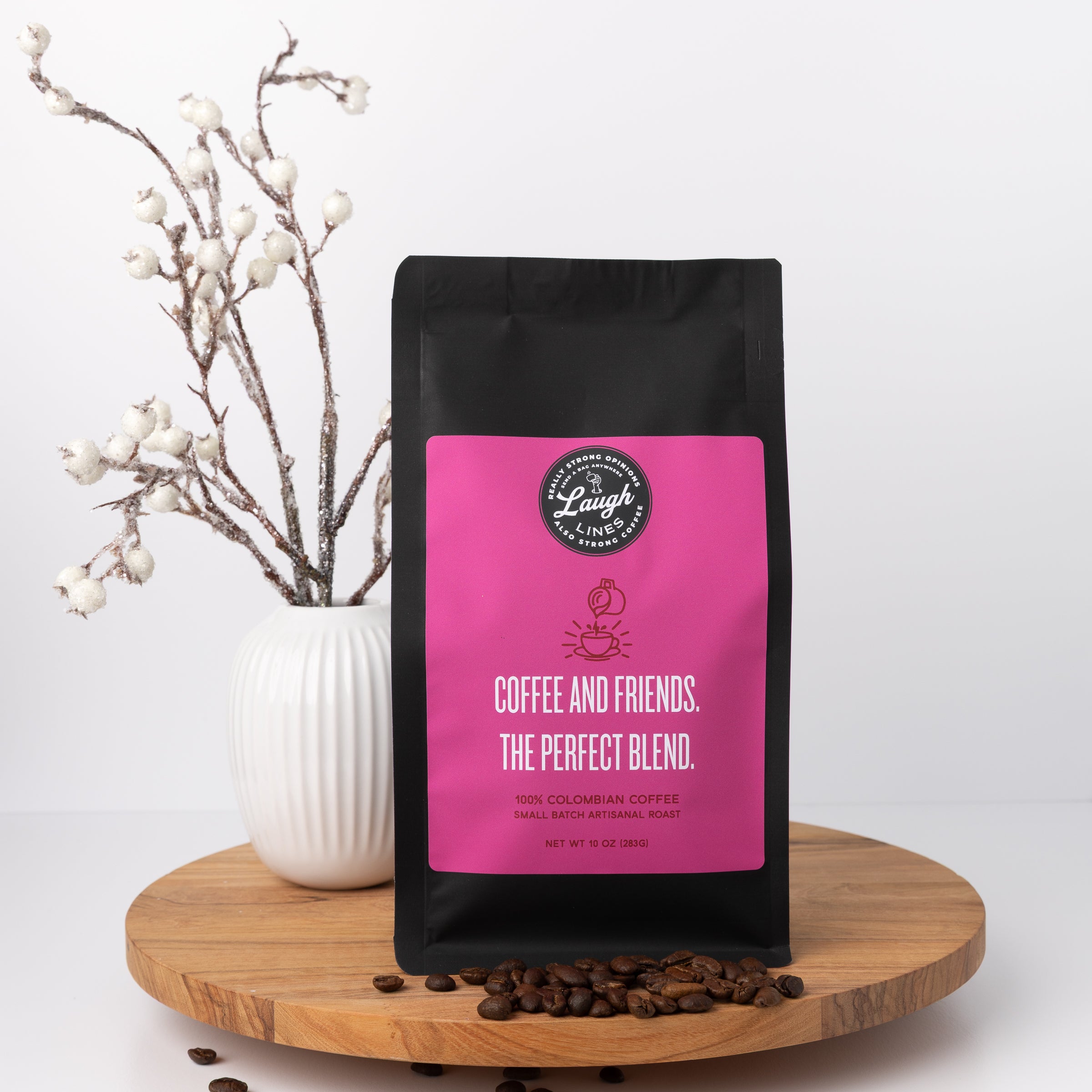 Coffee bag with pink label that reads 'Coffee and Friends. The Perfect Blend' on a wooden surface with coffee beans and a vase in the background