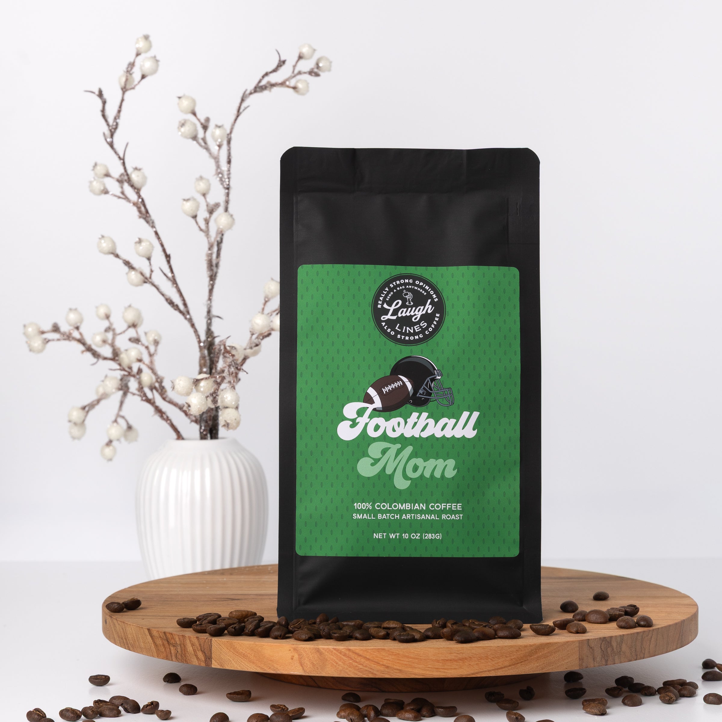 Coffee bag with 'Football Mom' design on a wooden surface with coffee beans and a decorative plant.