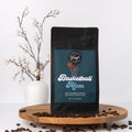 Coffee bag labeled 'Basketball Mom' on a wooden platform with coffee beans and a vase in the background.