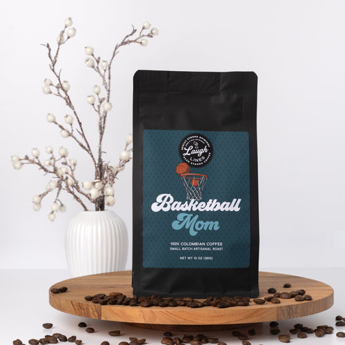 Coffee bag labeled 'Basketball Mom' on a wooden platform with coffee beans and a vase in the background.