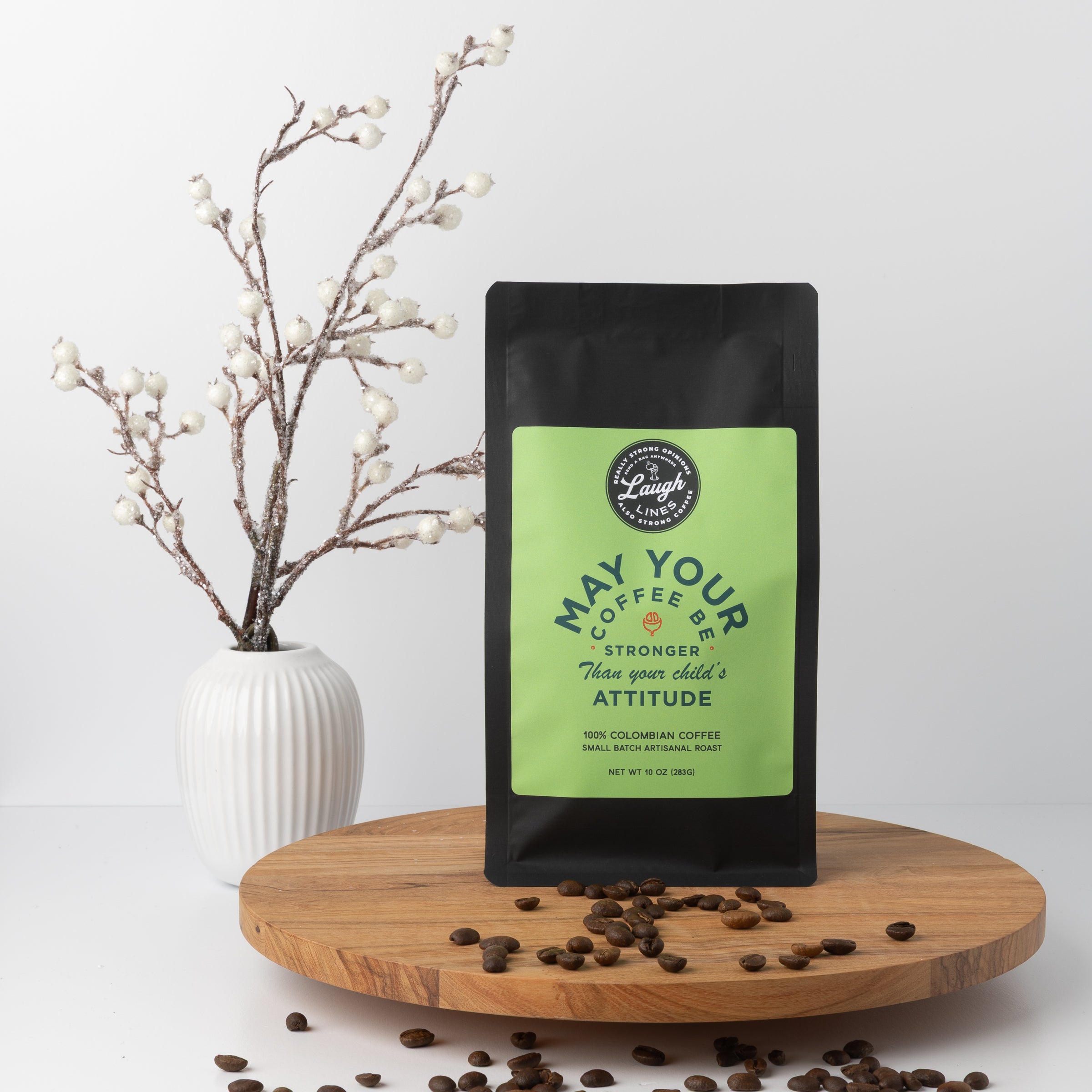 Coffee bag with humorous text that reads 'May Your Coffee be Stronger than Your Child's Attitude' on a wooden surface with coffee beans and a vase in the background