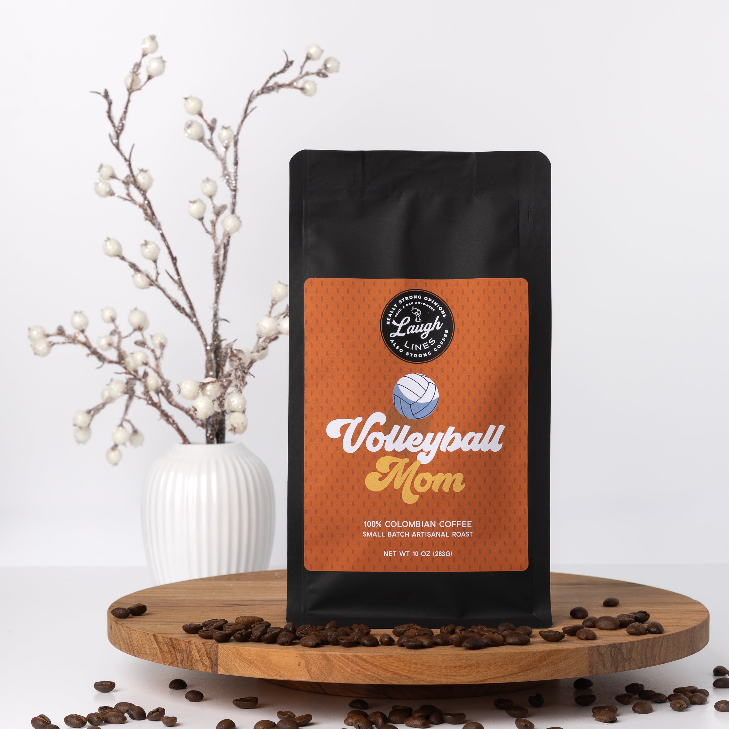Coffee bag labeled 'Volleyball Mom' on a wooden platform with coffee beans and decorative elements.