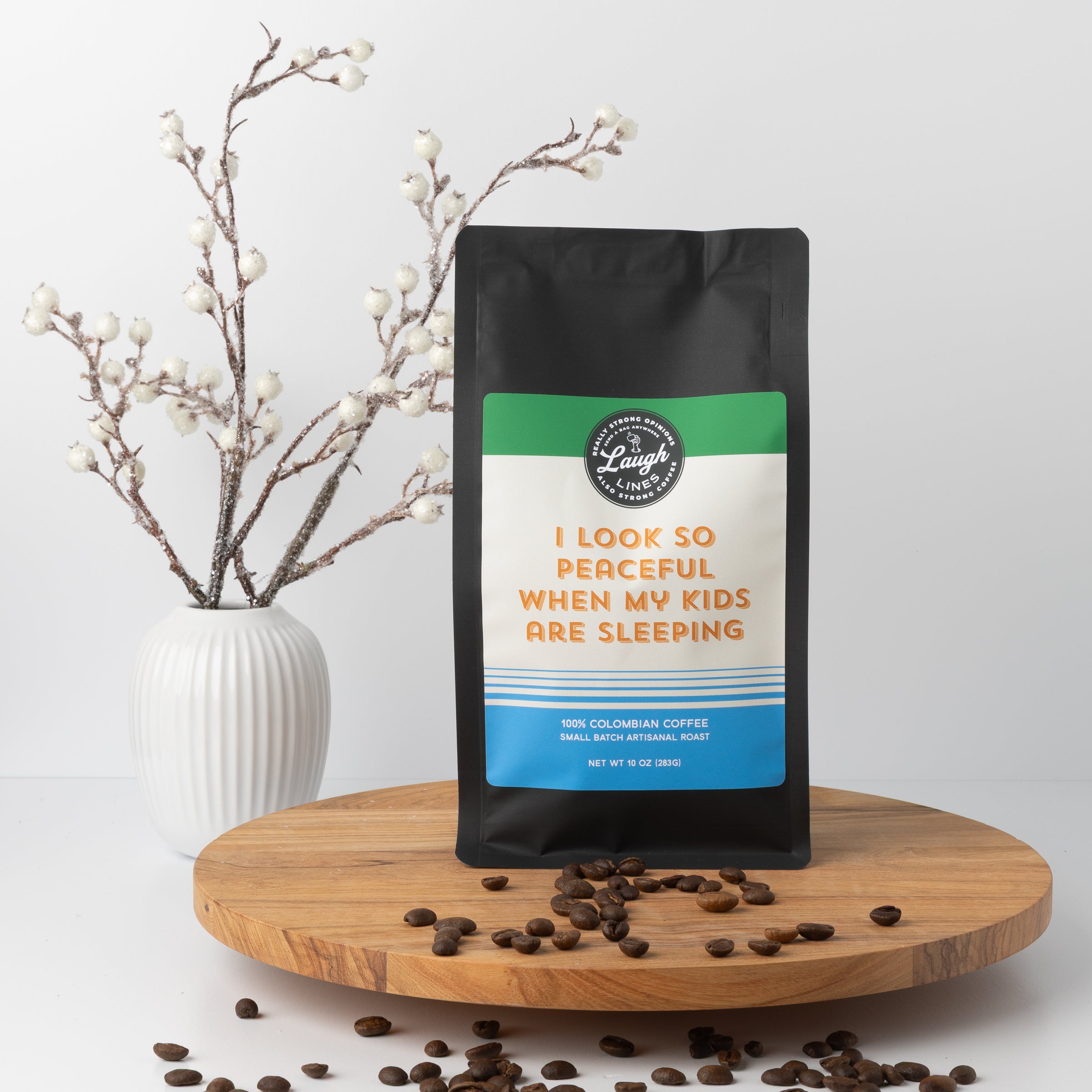 Coffee bag with humorous text that reads 'I Look so Peaceful When My Kids are  Sleeping' on a wooden surface with coffee beans and a vase in the background