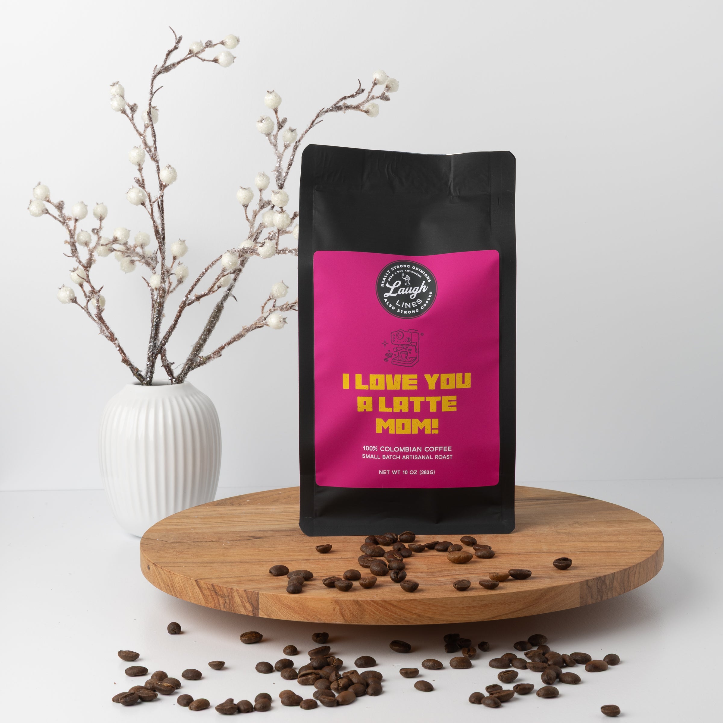 Coffee bag with 'I Love You a Latte Mom!' text on a wooden platform with coffee beans and a vase in the background.