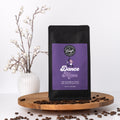 Coffee bag labeled 'Dance Mom' on a wooden tray with coffee beans and a vase in the background.