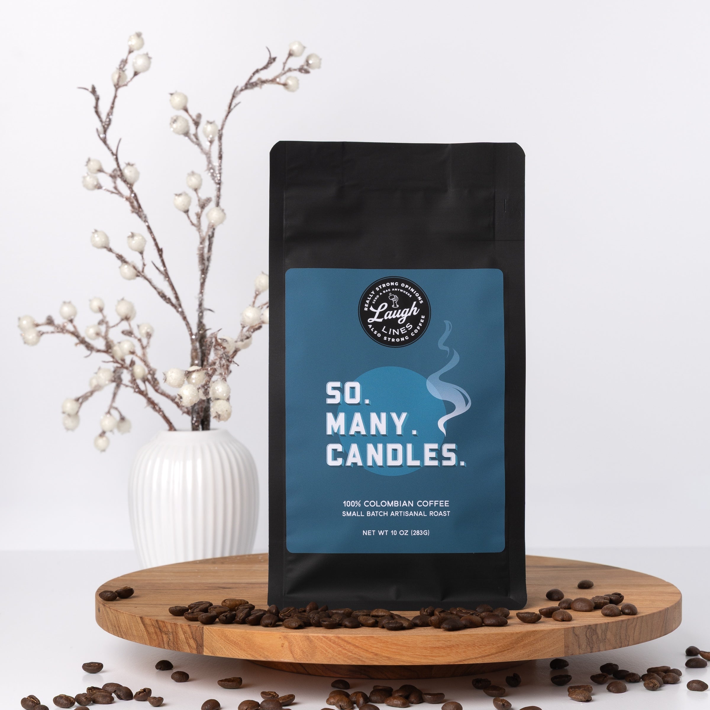 Coffee bag with 'So Many Candles' label on a wooden platform with coffee beans and a vase in the background.