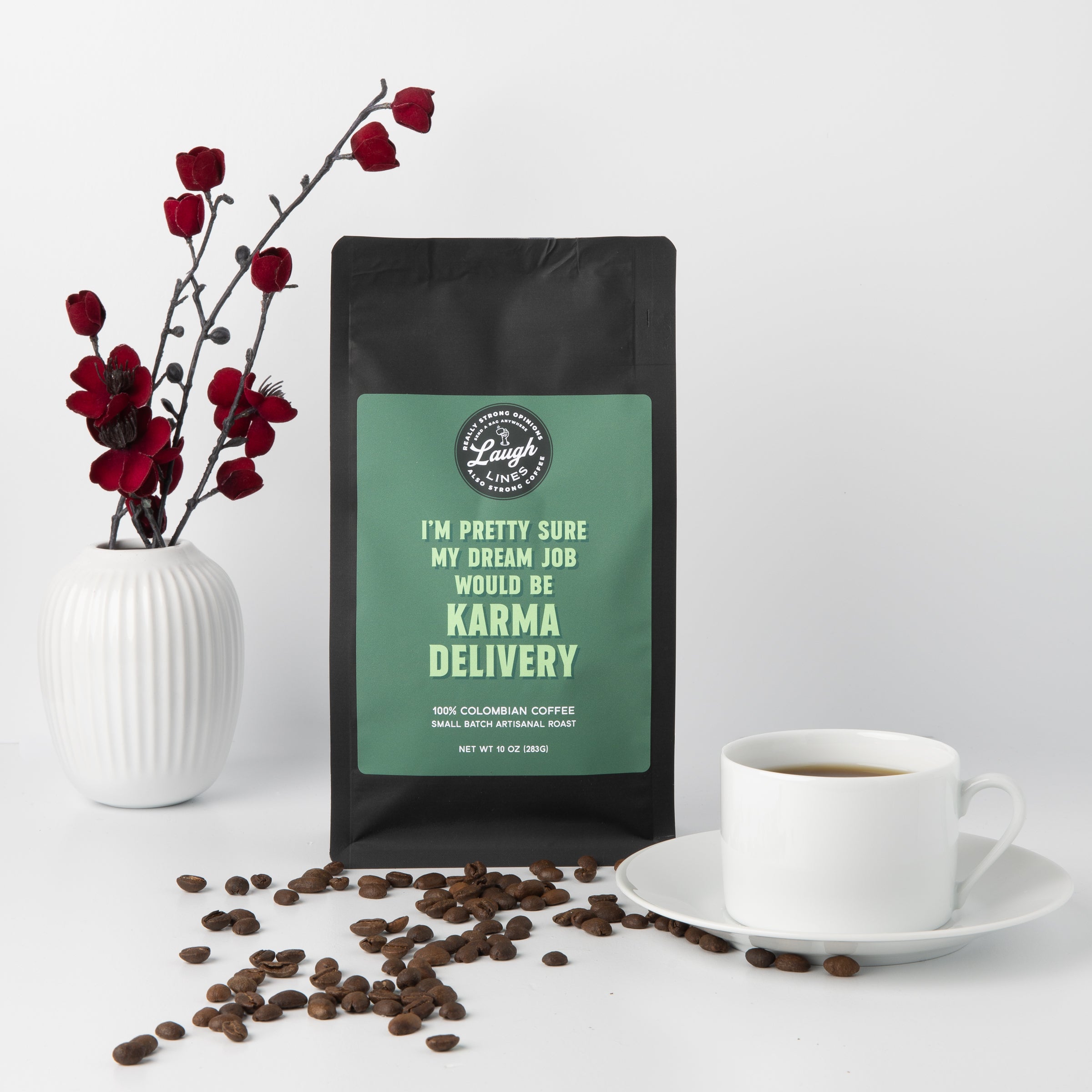 Coffee bag with humorous text that reads 'I'm Pretty Sure My Dream Job Would Be Karma Delivery', coffee beans, a cup of coffee, and red flowers on a white background
