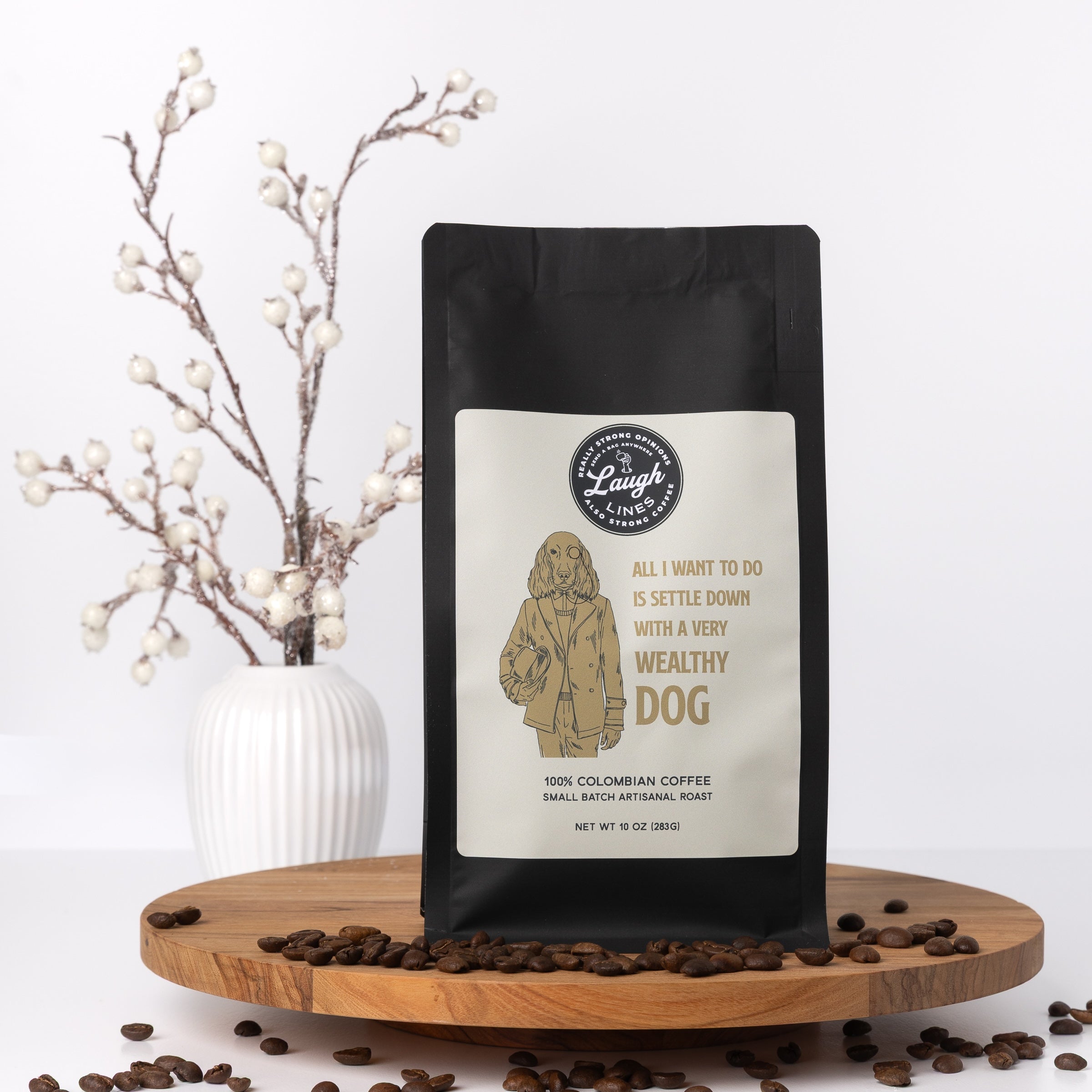 Coffee bag with a label that says "All I Want to Do is Settle Down with a Very Wealthy Dog" on a wooden stand with coffee beans and decorative branches.
