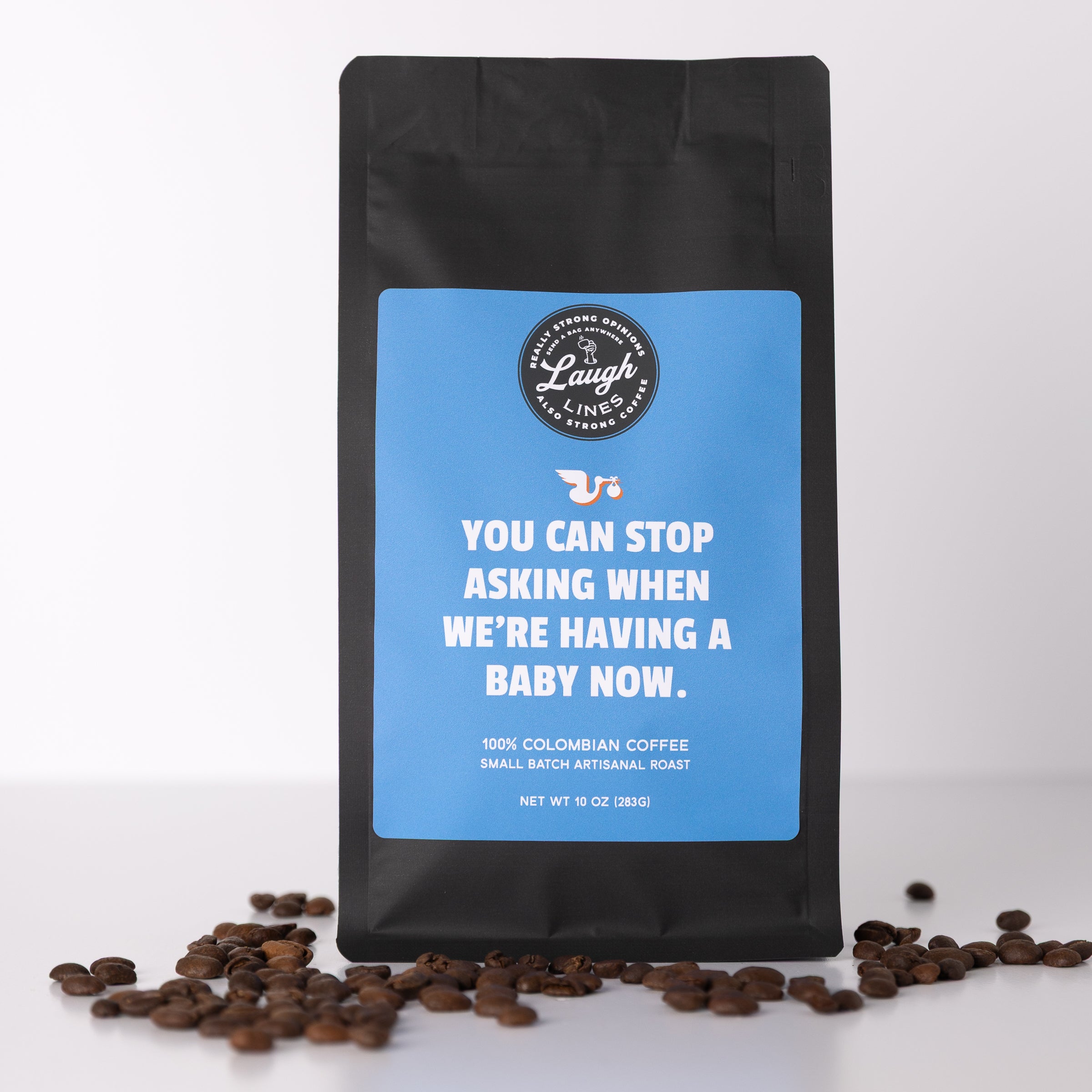 Coffee bag with blue label and black text that says 'You Can Stop Asking When We're Having a Baby Now,' surrounded by coffee beans on a white background