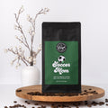 Coffee bag labeled 'Soccer Mom' on a wooden platform with coffee beans and decorative branches.